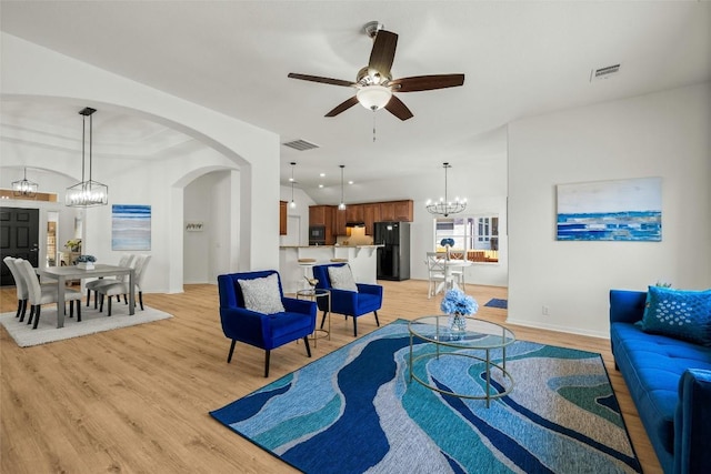 living area featuring visible vents, arched walkways, light wood-style floors, and ceiling fan with notable chandelier