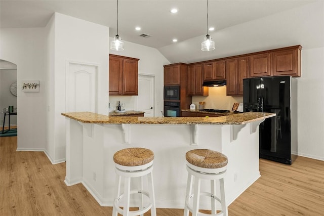 kitchen with under cabinet range hood, stone counters, arched walkways, and black appliances