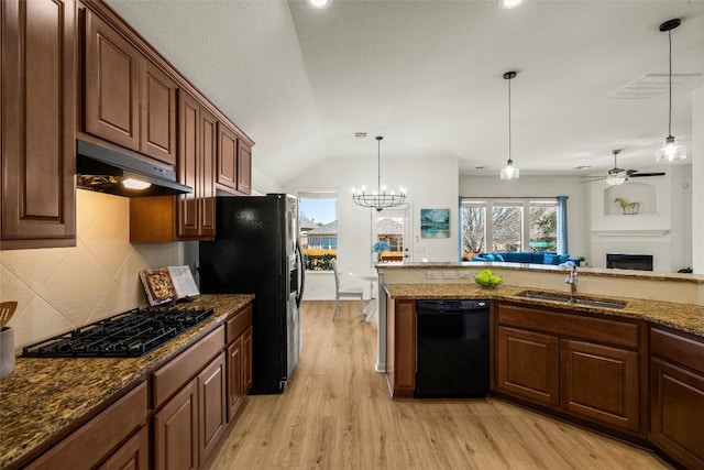 kitchen featuring light wood-type flooring, black appliances, under cabinet range hood, a sink, and a fireplace