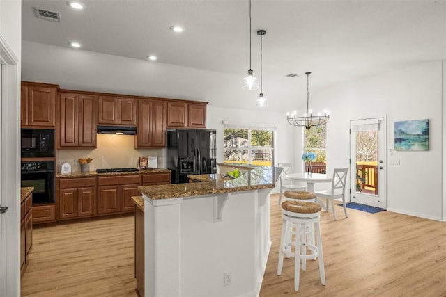 kitchen featuring under cabinet range hood, light wood-style flooring, black appliances, and a kitchen bar