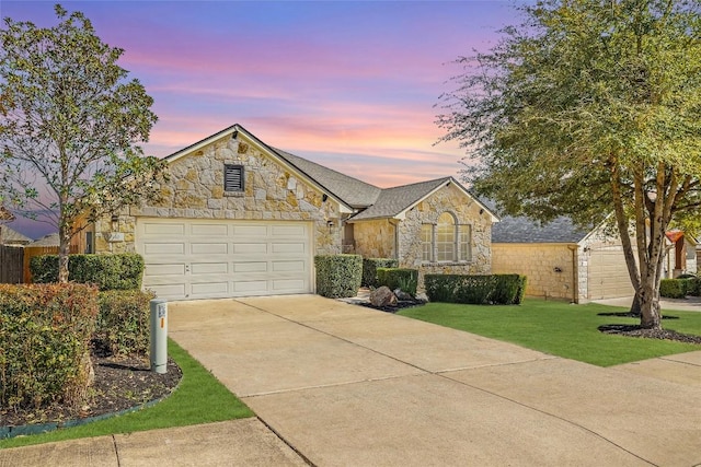 view of front facade with a garage, a yard, stone siding, and driveway