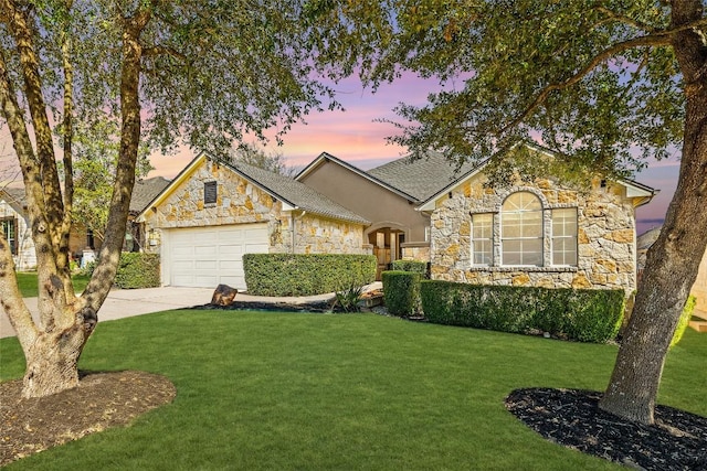 view of front facade with an attached garage, a shingled roof, concrete driveway, stone siding, and a lawn