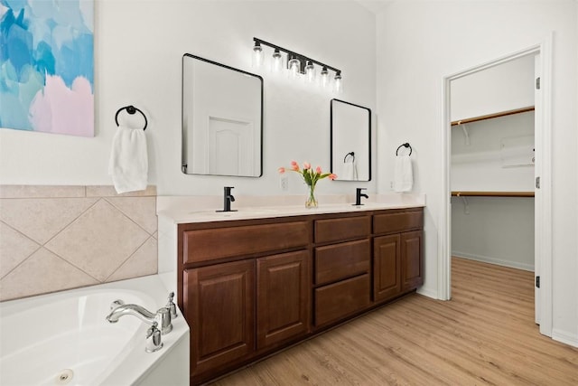 bathroom with a sink, wood finished floors, double vanity, and a bath