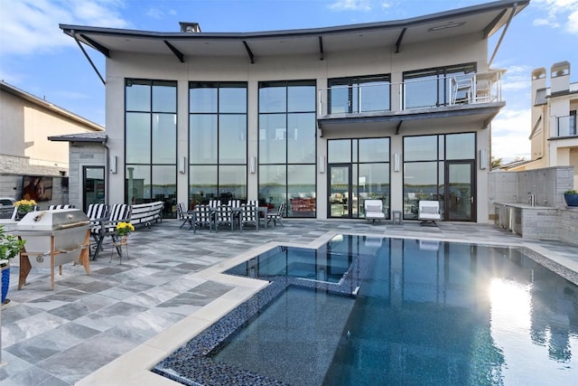 rear view of property with a balcony, a pool with connected hot tub, and a patio