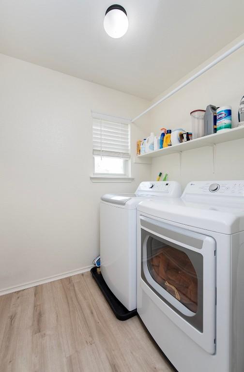 clothes washing area with laundry area, light wood-style floors, baseboards, and washing machine and clothes dryer