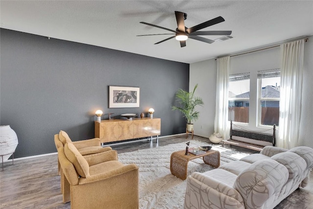 living room with wood finished floors, a ceiling fan, baseboards, and visible vents