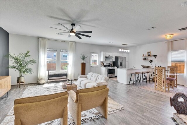 living area featuring visible vents, light wood-style flooring, a textured ceiling, and a ceiling fan