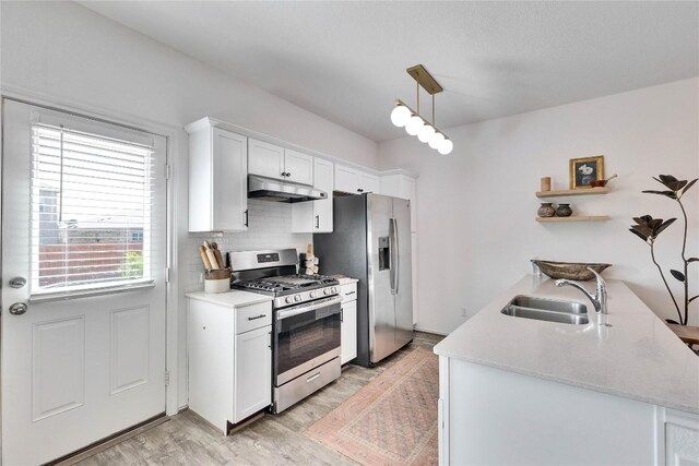 kitchen with a sink, stainless steel appliances, white cabinets, under cabinet range hood, and tasteful backsplash