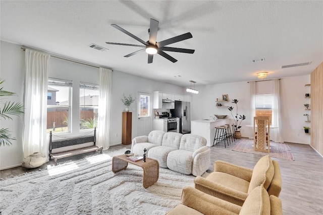 living room featuring light wood-type flooring, visible vents, and a ceiling fan