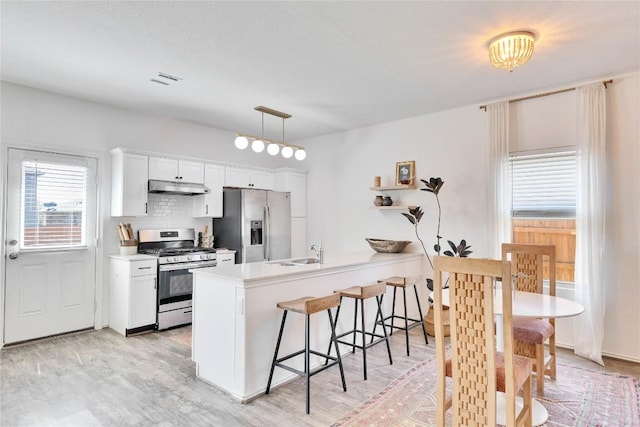 kitchen with a breakfast bar, under cabinet range hood, stainless steel appliances, a peninsula, and white cabinets