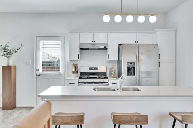 kitchen featuring tasteful backsplash, under cabinet range hood, a kitchen bar, stainless steel appliances, and a sink