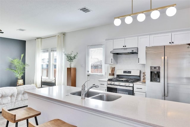 kitchen featuring a sink, under cabinet range hood, appliances with stainless steel finishes, white cabinetry, and backsplash