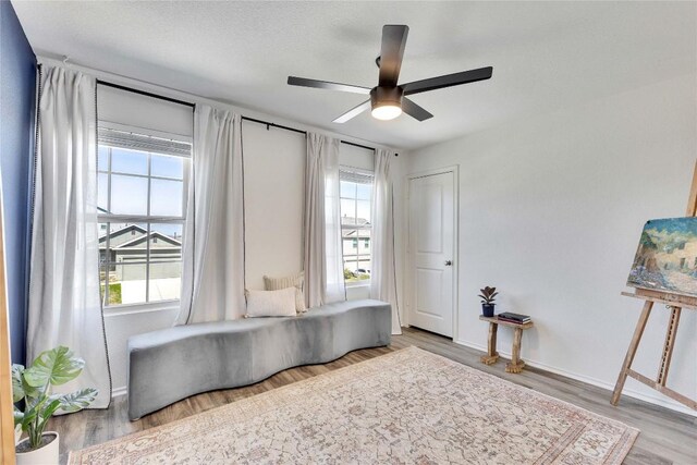 living area with baseboards, ceiling fan, and wood finished floors