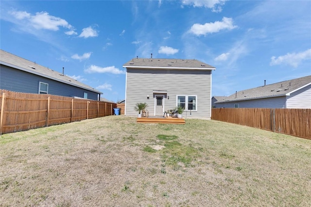 back of property with a fenced backyard, a deck, and a yard