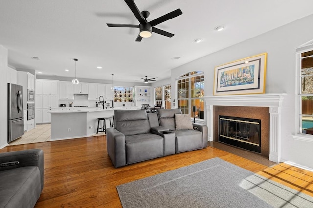 living room with recessed lighting, a glass covered fireplace, light wood-style flooring, and ceiling fan