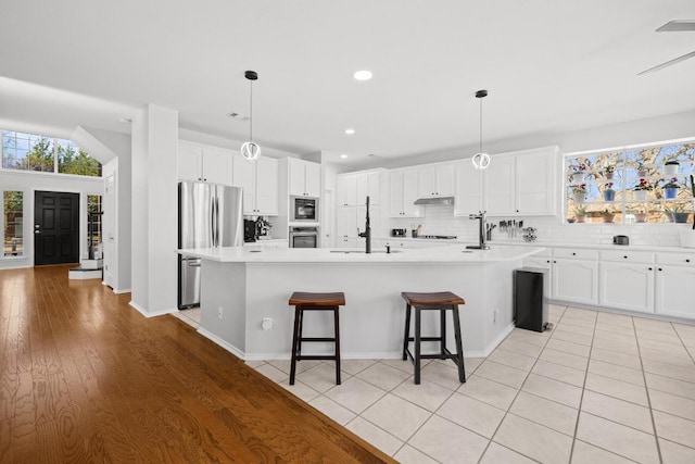 kitchen featuring under cabinet range hood, tasteful backsplash, appliances with stainless steel finishes, and white cabinetry