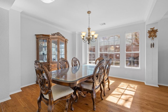 dining space with visible vents, light wood-style floors, an inviting chandelier, crown molding, and baseboards