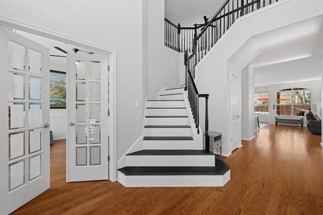 stairway with french doors, a high ceiling, and wood finished floors