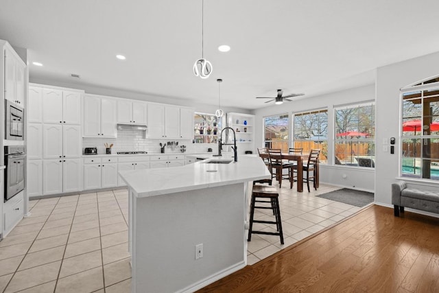 kitchen featuring under cabinet range hood, light tile patterned flooring, stainless steel appliances, a ceiling fan, and a sink