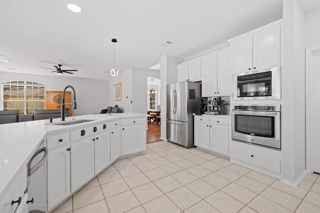 kitchen with open floor plan, ceiling fan with notable chandelier, white cabinets, stainless steel appliances, and a sink