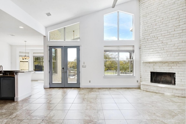 unfurnished living room featuring a brick fireplace, french doors, baseboards, and a wealth of natural light