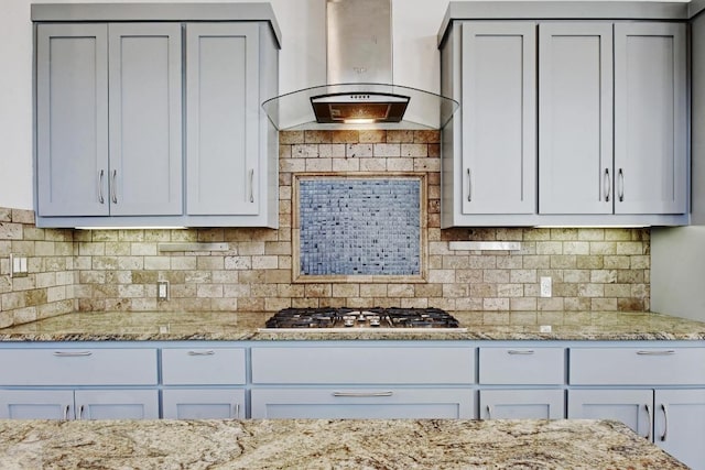 kitchen featuring stainless steel gas cooktop, backsplash, ventilation hood, and light stone countertops