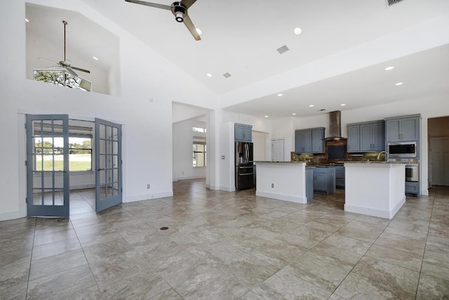 kitchen featuring a kitchen island with sink, french doors, stainless steel appliances, wall chimney exhaust hood, and ceiling fan