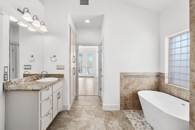 bathroom featuring a freestanding tub, visible vents, tile walls, and vanity