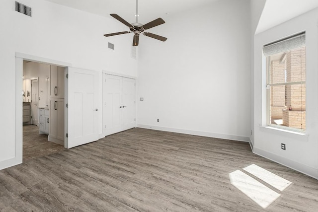 unfurnished bedroom with visible vents, a high ceiling, baseboards, and wood finished floors