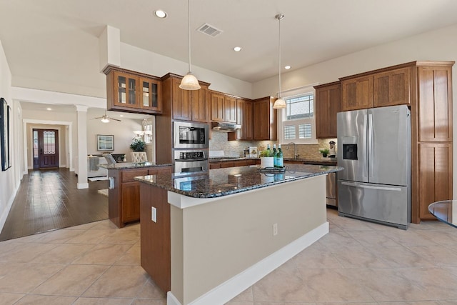 3129 Mill Stream Dr, Cedar Park, TX 78613 - kitchen featuring stainless steel appliances, dark stone countertops, decorative backsplash, a kitchen island, and brown cabinets
