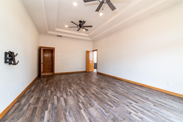 spare room featuring visible vents, a tray ceiling, wood finished floors, baseboards, and ceiling fan