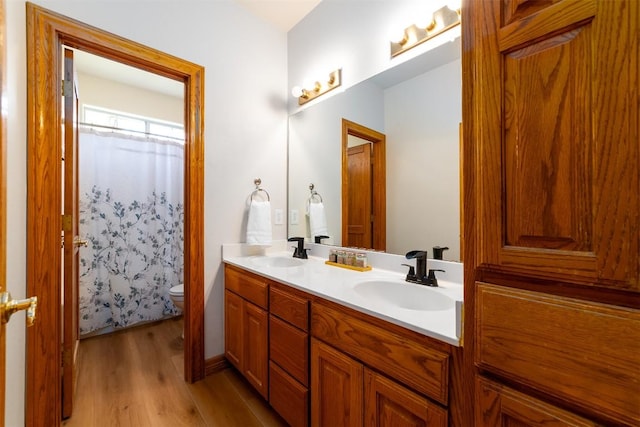 bathroom with double vanity, wood finished floors, toilet, and a sink