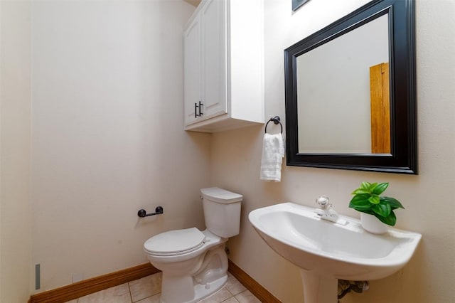 half bathroom featuring tile patterned flooring, toilet, baseboards, and a sink