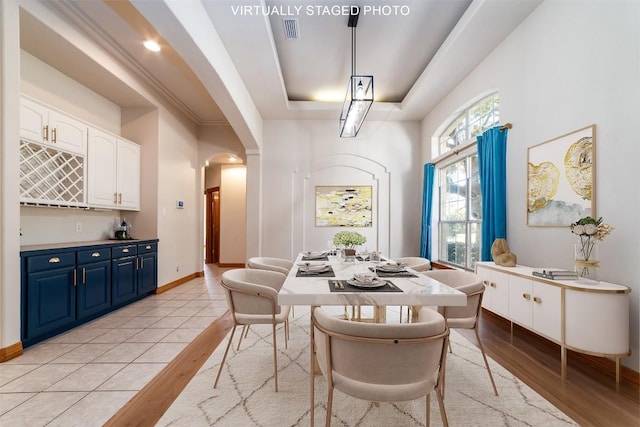 dining room featuring visible vents, baseboards, arched walkways, light wood-style floors, and a raised ceiling