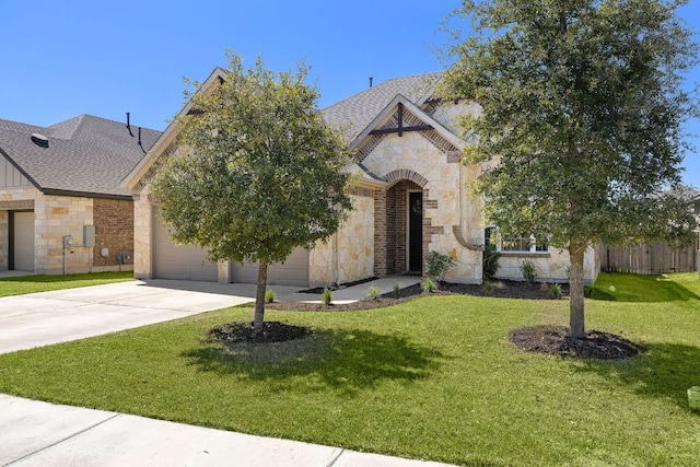 view of front facade with driveway, stone siding, an attached garage, a shingled roof, and a front yard