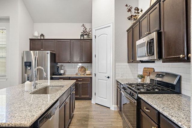 kitchen with dark brown cabinetry, light wood-style flooring, appliances with stainless steel finishes, and a sink