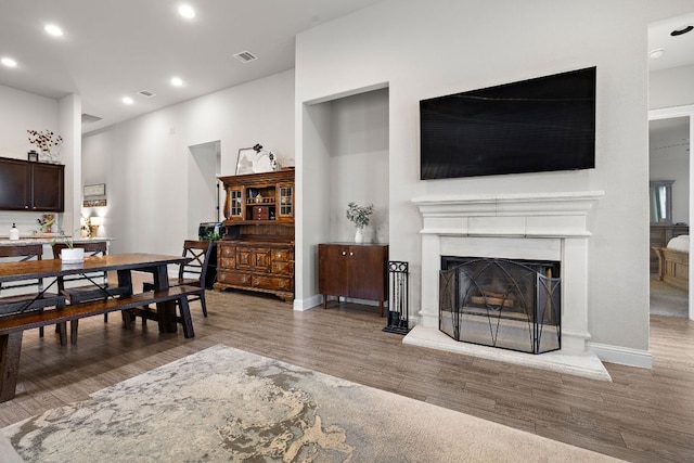 dining room featuring visible vents, a fireplace with raised hearth, baseboards, recessed lighting, and wood finished floors