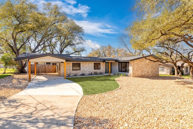 mid-century modern home featuring fence, concrete driveway, a front yard, a carport, and stone siding