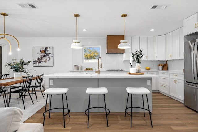 kitchen featuring stainless steel refrigerator, wood finished floors, visible vents, and a sink