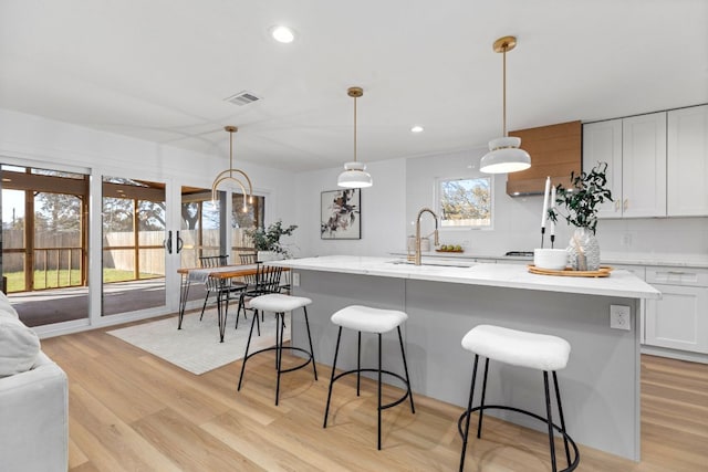 kitchen with white cabinets, a kitchen bar, light wood-style floors, and a sink