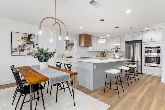 kitchen with visible vents, custom range hood, stainless steel appliances, a breakfast bar area, and light countertops