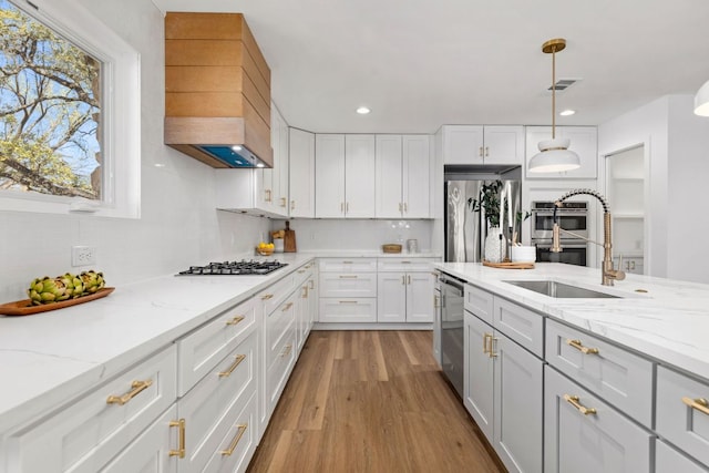 kitchen with premium range hood, a sink, backsplash, wood finished floors, and appliances with stainless steel finishes