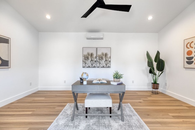 office space featuring baseboards, light wood finished floors, a ceiling fan, and a wall unit AC