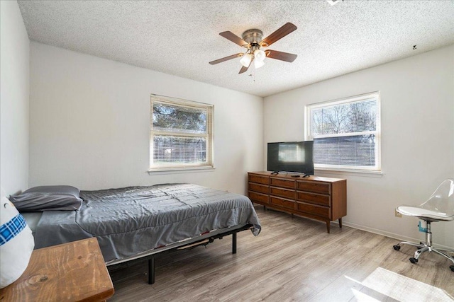 bedroom with ceiling fan, wood finished floors, baseboards, and a textured ceiling