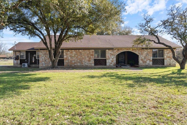 back of property with a lawn, stone siding, and roof with shingles