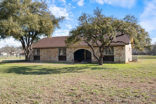 view of front of house with stone siding, roof with shingles, and a front lawn