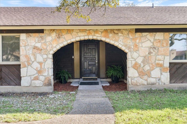 doorway to property with stone siding and roof with shingles