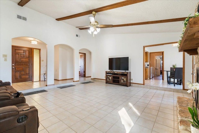 living area with arched walkways, light tile patterned floors, vaulted ceiling with beams, and a ceiling fan