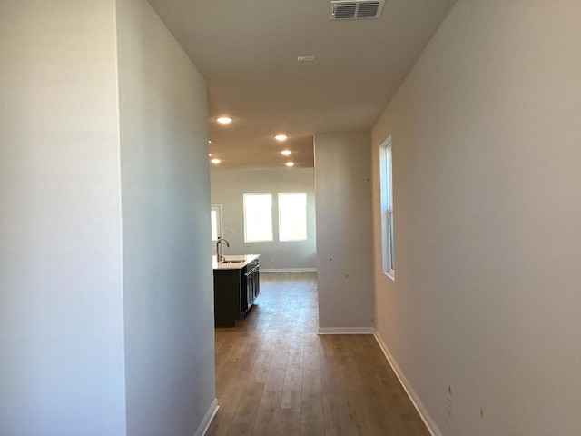 hall with wood finished floors, visible vents, baseboards, recessed lighting, and a sink