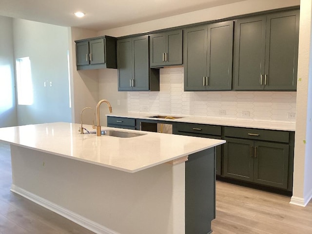 kitchen featuring a sink, black electric stovetop, light countertops, light wood-style floors, and a kitchen island with sink